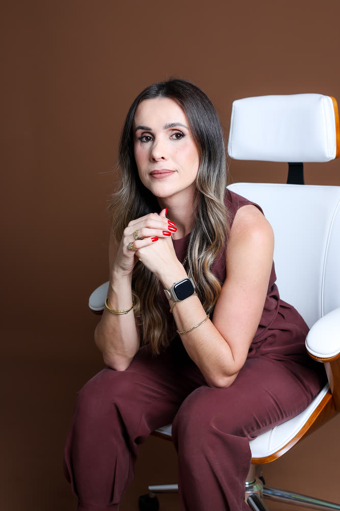 Retrato profissional de uma mulher em uma cadeira branca, com fundo marrom, em estúdio